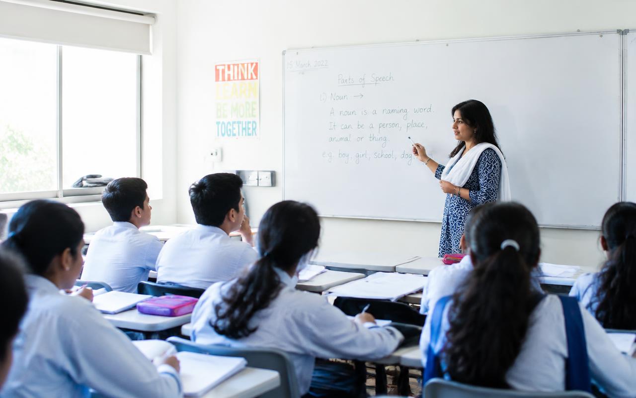 NAS Academy teacher explaining a lesson to students in a bright classroom